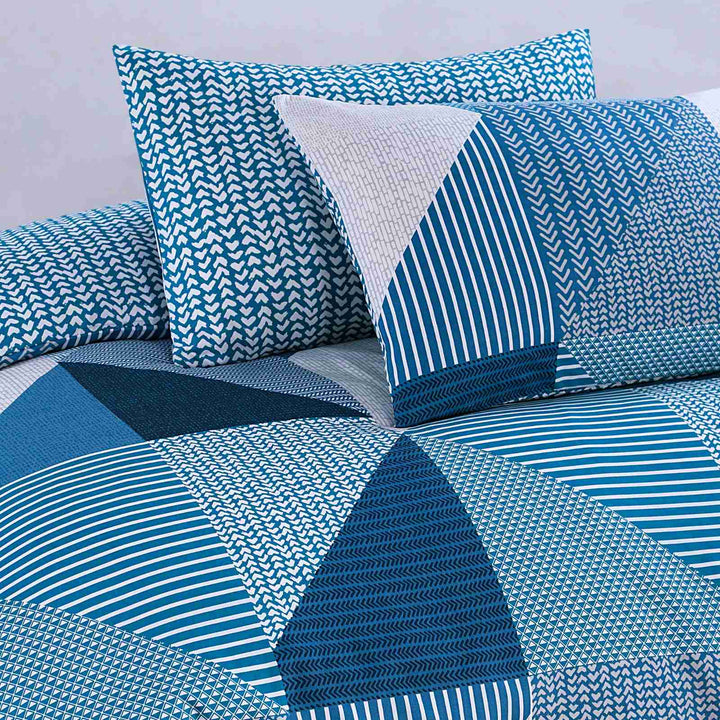 Blue and white geometric patterned bedding set on a bed with pillows.